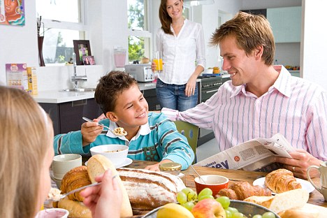 Family having breakfast at kitchen table, mother standing in background