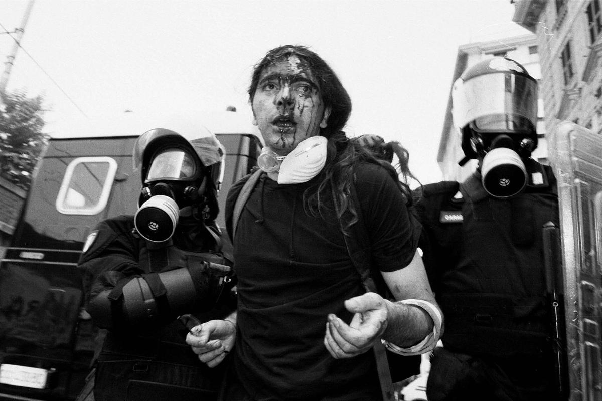 Genova, piazza affollata con manifestanti in corteo, striscioni e bandiere, città storica sullo sfondo