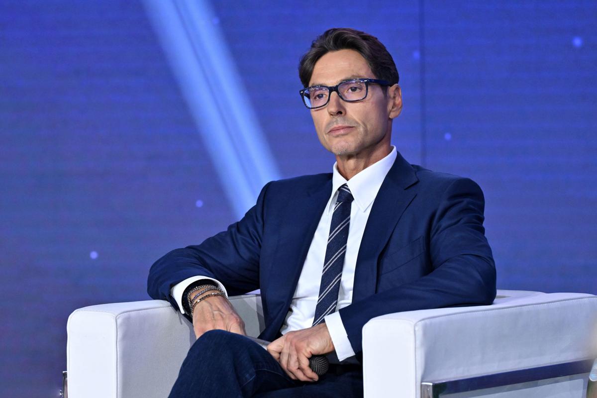 Riunione aziendale con dirigenti Mediaset, documenti su scrivania, organigamma strategico in background