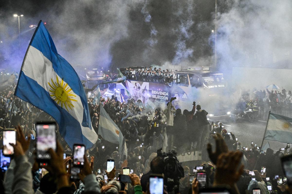 Aeroporto internazionale con scritta celebrativa, squadra calcio argentina che scende da aereo, tifosi sotto la pioggia, immagine di approfondimento
