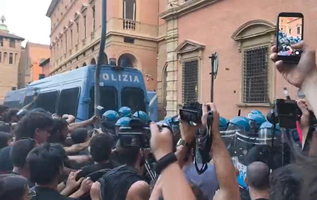 Piazza affollata con corteo e forze dell'ordine in assetto antisommossa, idranti e lacrimogeni in azione, immagine di approfondimento