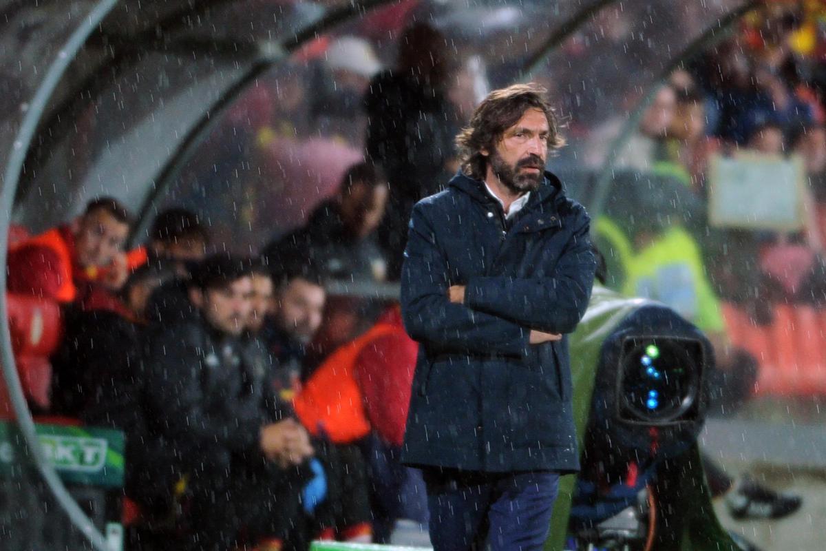 Andrea Pirlo in panchina durante una partita, volto concentrato, sullo sfondo lo stemma della Nazionale italiana
