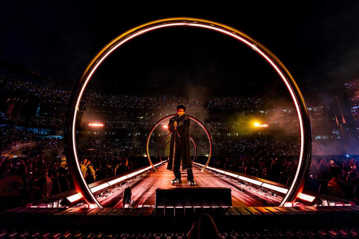 Palco illuminato allo stadio San Siro con performer al centro tra effetti visivi futuristici e pubblico in platea