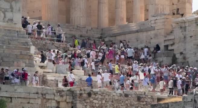 Volontari della Croce Rossa distribuiscono bottiglie d'acqua a turisti presso l'Acropoli di Atene sotto il sole intenso, immagine di approfondimento