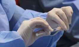 Mani in guanti medici tengono una siringa con liquido.
