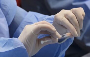 Mani in guanti medici tengono una siringa con liquido.