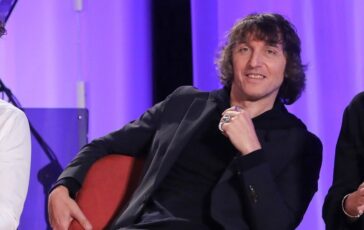 Giuseppe Cruciani seduto su un divano rosso durante un'intervista televisiva