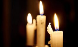 Tre candele accese su sfondo scuro, una con fiamma più grande.