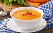 Ciotola di vellutata di zucca cremosa con decorazioni di semi e peperoni su piatto bianco