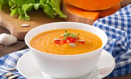 Ciotola di vellutata di zucca cremosa con decorazioni di semi e peperoni su piatto bianco