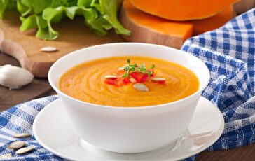 Ciotola di vellutata di zucca cremosa con decorazioni di semi e peperoni su piatto bianco