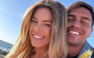 Primo piano di Sophie Codegoni con capelli biondi e Alessandro Basciano che sorridono felici all'aperto, con il mare sullo sfondo